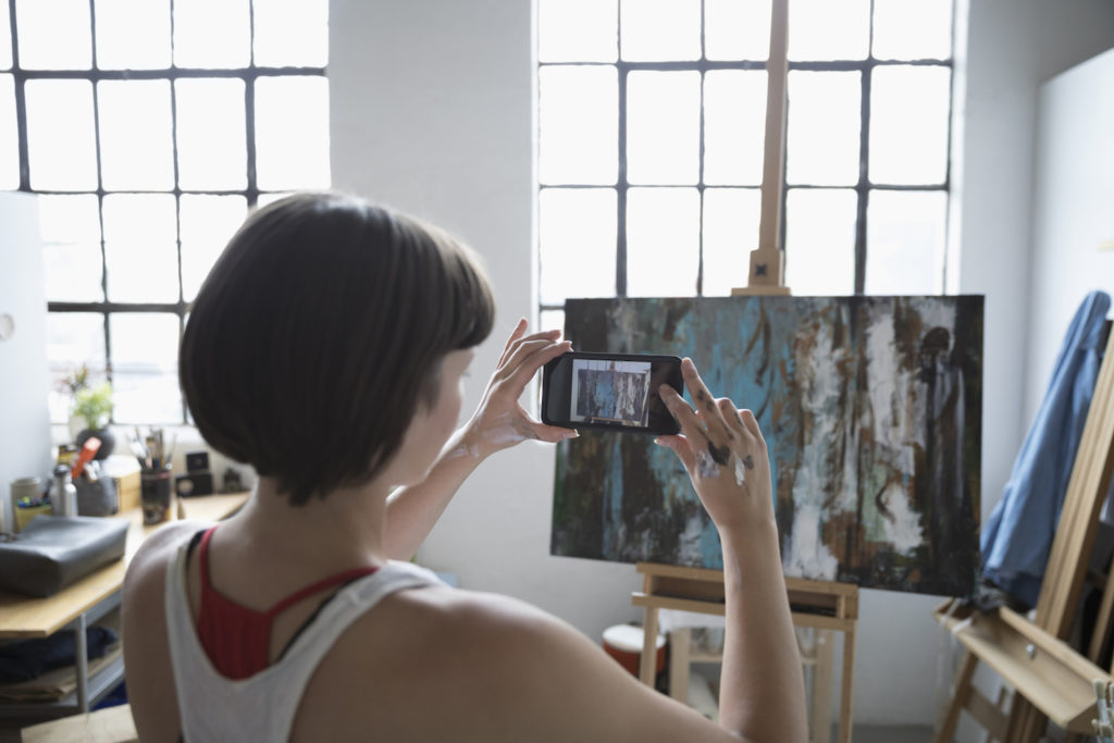 Artist taking picture of painting, photo courtesy of Getty Images | how to sell art online -- article by Artists Network